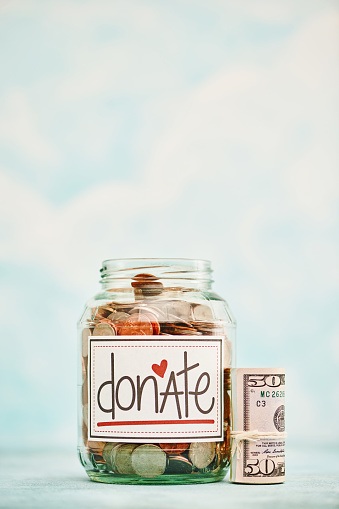 Donation jar filled with American currency and a wad of fifty dollar bills against a bright background with lots of copy space