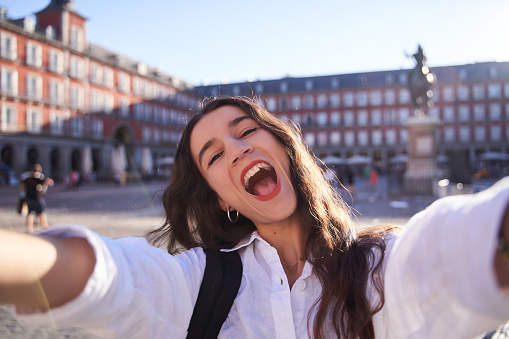 Happy caucasian woman is taking a selfie smiling at the camera in front of the Equestrian Monument to King Felipe III of Spain in the Plaza Mayor in Madrid