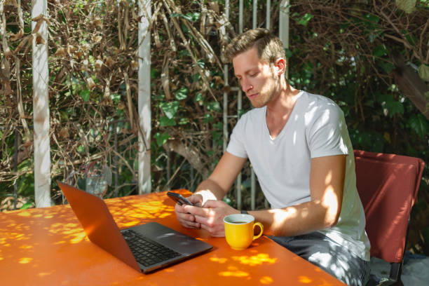 istock Young Man working with laptop outdoor in a beautiful terrace using smartphone and computer sitting cross-legged in Home work. 1407195026