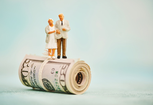 Miniature figures of elderly couple standing on top of a wad of fifty dollar bills
