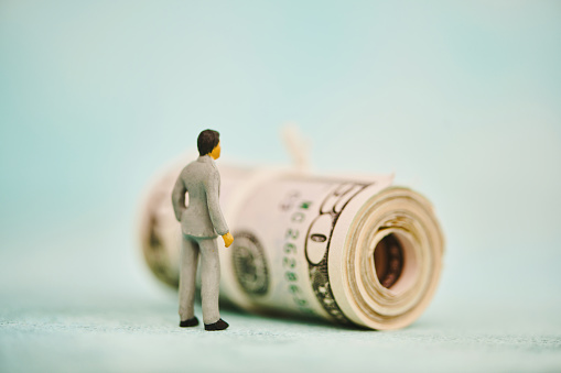Miniature figure of a businessman looking at a wad of fifty dollar bills