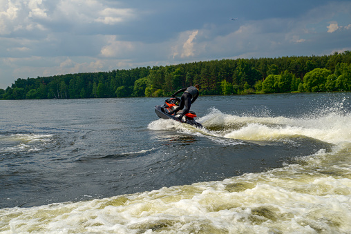A man on a jet ski on the Klyazminsky or Pirogovsky reservoir Sunny summer day in the suburbs! (unrecognizable person). Splash from water sports - a man makes a turn on a jet ski. Airplane in the sky moves to Sheremetyevo airport