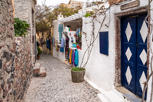 Oia, Santorini, Greece, Apr. 2022 – Scenic alley with a shop selling colorful clothes and handicraft products