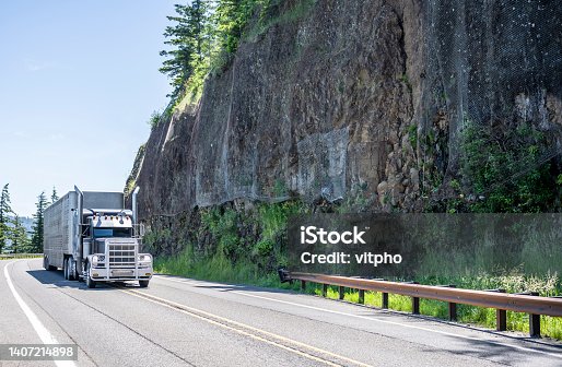 istock Black classic American big rig semi truck with grille guard and chrome parts transporting animal semi trailer driving on the winding mountain highway road 1407214898