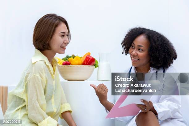 African American Nutritionist With Bowl Of Variety Of Fruit And Vegetable Giving Advice To The Client For Healthy Diet And Vitamin Booster Concept Stock Photo - Download Image Now