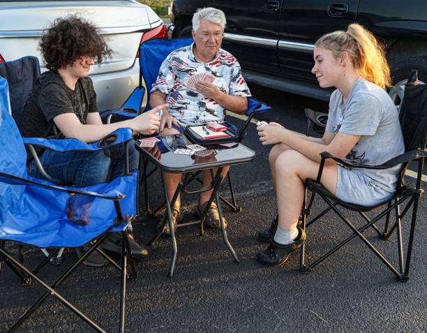 Grandfather Plays Cards with Grandchildren A grandfather plays cards with his teen-aged granddaughter and grandson outdoors while they wait for an event to begin. people family tailgate party outdoors stock pictures, royalty-free photos & images