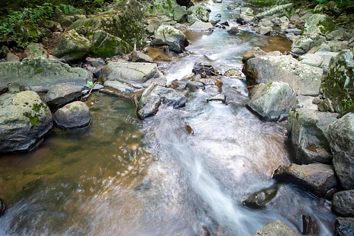 Closeup of long exposure stream flowing around large gray stones and boulders. Water flows away from the camera in a stream nature background. Natural light with no people and copy space.