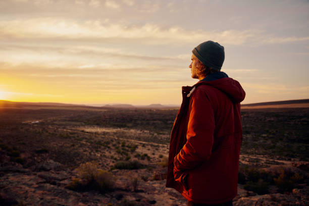 istock Thoughtful man wearing jacket and cap standing on mountain looking at morning sunrise 1407238164