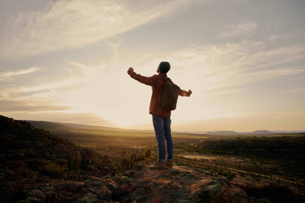 istock Young man with backpack standing on mountain with hands outstretched 1407238254