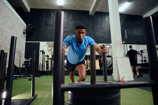 African American man working out intensely during gym training. Male athlete pushing the sled in the gym. High quality photo