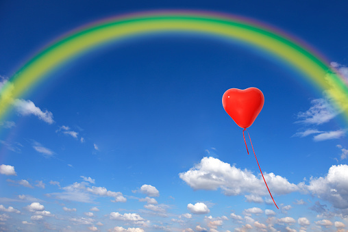 One red heart-shaped balloon floating in a blue sky with copy space.