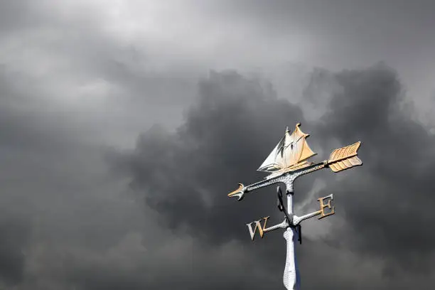 Photo of Sailboat weather vane against storm clouds