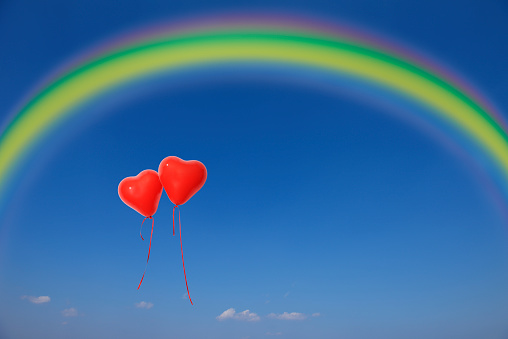 Two red heart-shaped balloons floating in a blue sky with copy space.