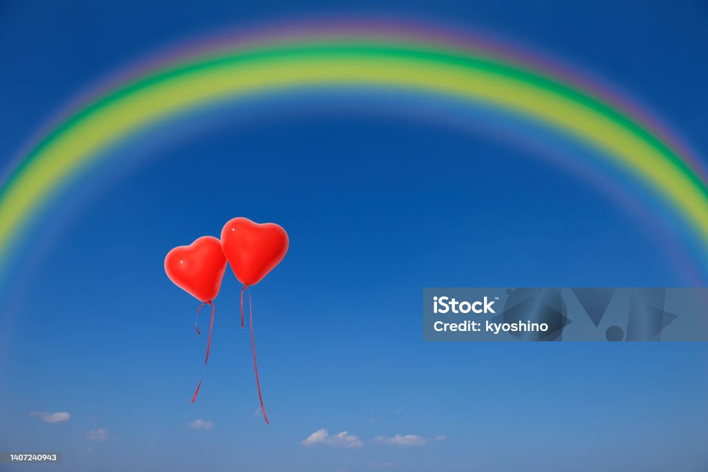 Two red heart-shaped balloons floating in a blue sky with a rainbow Two red heart-shaped balloons floating in a blue sky with copy space. Abstract Stock Photo