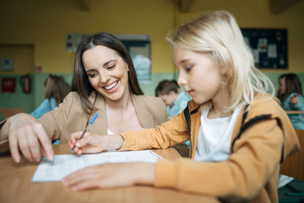 istock Schoolboy asking doubt to teacher while studying at desk in classroom 1407241122