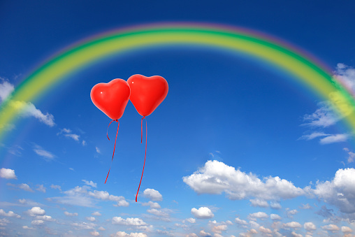 Two red heart-shaped balloons floating in a blue sky with copy space.