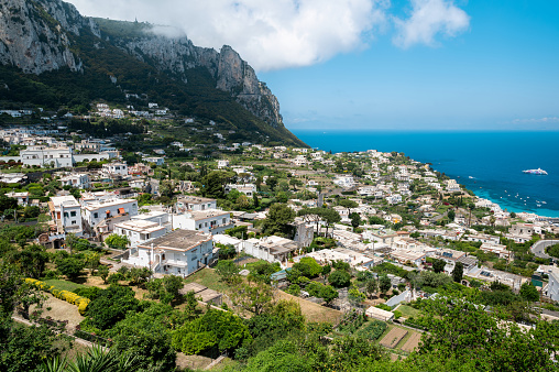 Cityscape of Capri, Italy. Rows of residential buildings, Tyrrhenian sea coast, greenery and rocky mountain. View from a hill