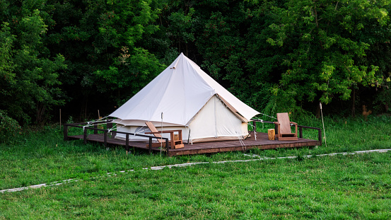 Tent with wooden chairs in front of it at glamping, lush forest around