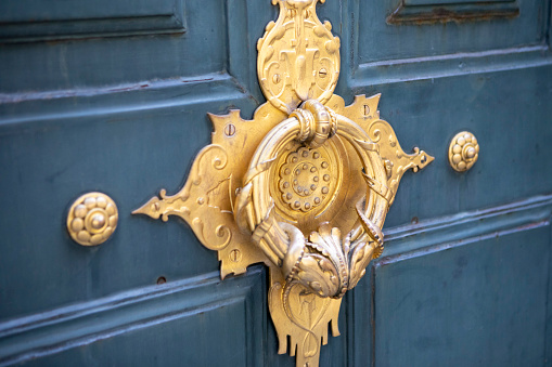 Close-up of an ornate gold coloured door knocker on a wooden door in Paris