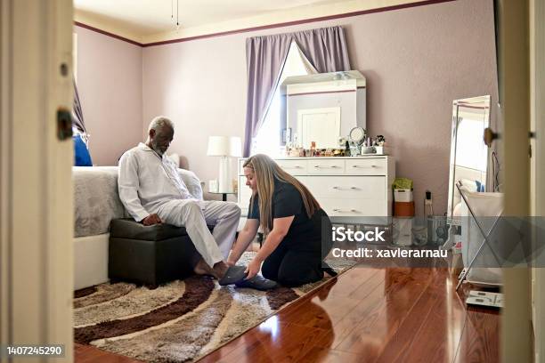 Early 70s Black Man Receiving Assistance With His Slippers Stock Photo - Download Image Now