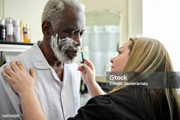Latin American Caregiver Shaving Senior Black Client Stock Photo - Download Image Now