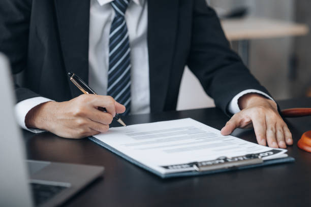 un abogado se sienta en su oficina, en una mesa con un pequeño martillo para golpear el escritorio de los jueces en la corte. y escalas de justicia, los abogados están redactando un contrato para que el cliente lo use con el acusado para firmar. - drafting fotografías e imágenes de stock