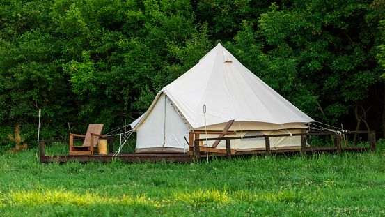 Tent with wooden chairs in front of it at glamping, lush forest around