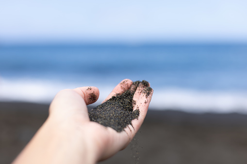 Black volcanic sand in the hand. Closeup.