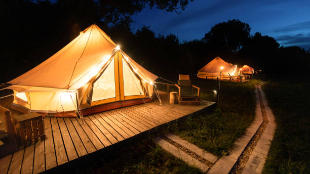 Tents at glamping, night Tents with burning torches, lamps and wooden chairs at glamping, forest around, night glamping photos stock pictures, royalty-free photos & images