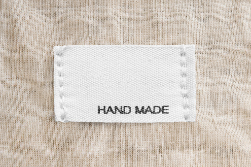 Clothing label says handmade on beige linen background