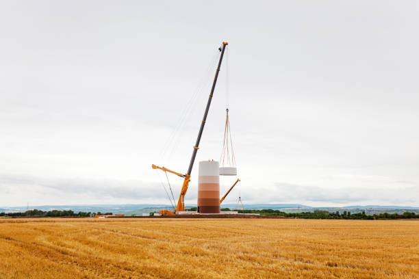 Energy saving concept from wind turbine construction in wheat field and meadow with mountain with cloudy sky background.