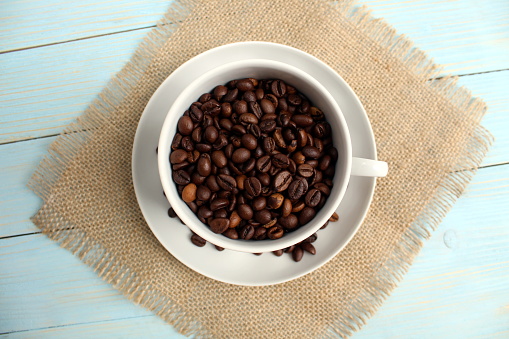A white cup stands with black coffee beans.
