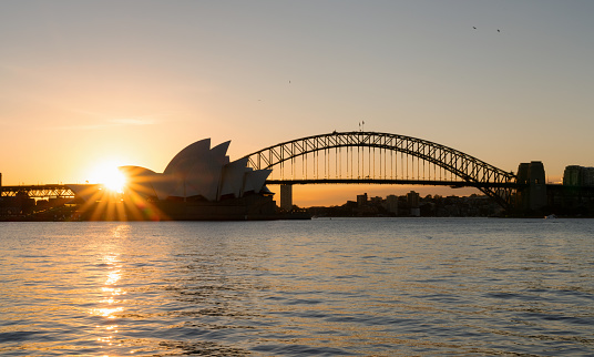 Sydney, Australia - August 3, 2019: Evening descends upon Sydney, and the twin icons of Sydney Harbour, the Opera House and the Harbour Bridge, stand out against a dramatic sky.