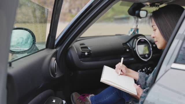 Woman with notebook sketching in car doorway