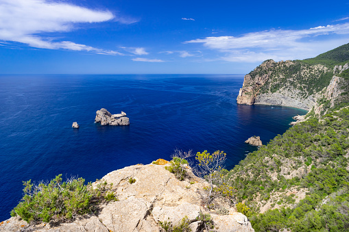 Wide-angle view of the mirador of Sa Penya Esbarrada, popularly known as Las Puertas del Cielo (Heaven’s Doors), which enjoys a wonderful vista on a long stretch of steep cliffs on the western coast of Ibiza. Deep blue waters as far as the eye can see, picturesque clouds, lush vegetation, the bright light of a summer noon. The vertiginous cliff of Ses Balandres can be seen on the right, the islet of Ses Margalides on the centre. Developed from RAW.