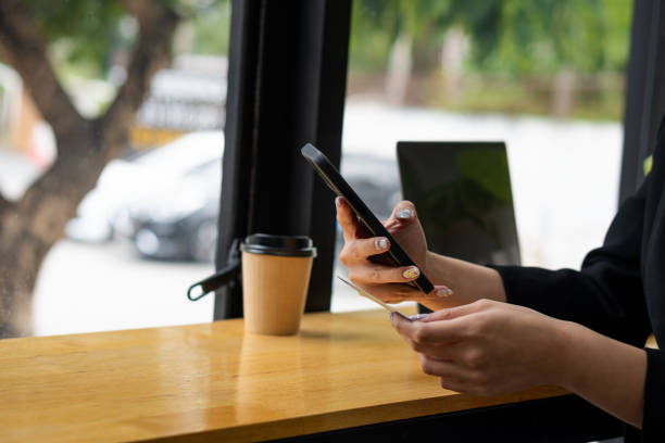 la mano di una giovane donna tiene accanto uno smartphone e un laptop e una tazza di caffè. - théâtre du châtelet foto e immagini stock