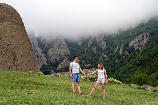 Happy man and woman holding hands and looking at each other on mountain pass. Mountain landscape in fog and cloudy weather.