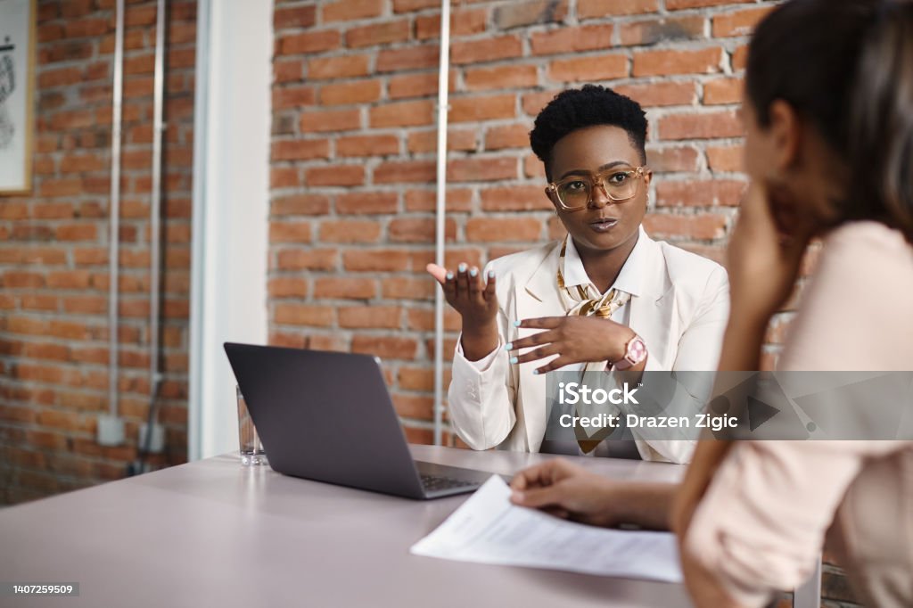 Black businesswoman talking to a candidate during job interview in the office. African American businesswoman communicating with female job candidate during a meeting in the office. Mentorship Stock Photo