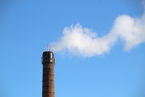 Thick effluent coming out of a tall chimney against a blue sky background. Composed to allow space for copy.