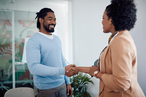 Happy African American man shaking hands with female member of human resource team after job interview in the office.