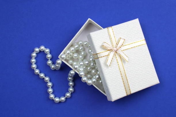 On a blue background lies a white gift box with a pearl necklace.