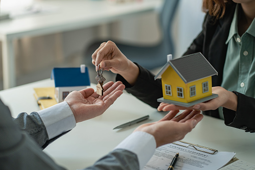 El gerente de ventas o agente de bienes raíces le da al cliente las llaves después de firmar el contrato de arrendamiento, o Comprar una casa con préstamo hipotecario y seguro de hogar en la oficina photo