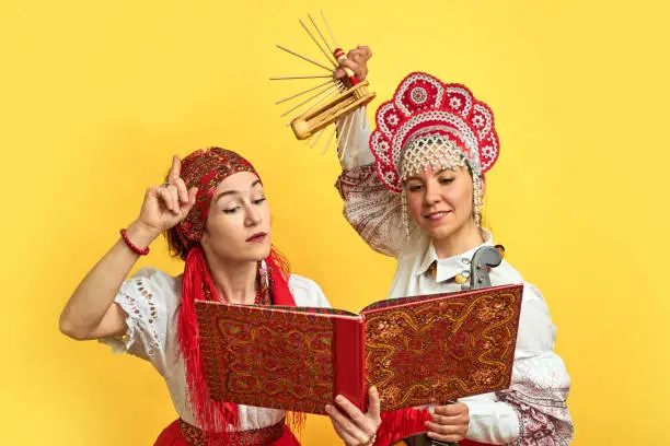 Photo of Women musicians in Russian folk dresses with musical instruments on a yellow studio background. Happy artists from Russia in national clothes with stringed musical instruments with smiles on faces