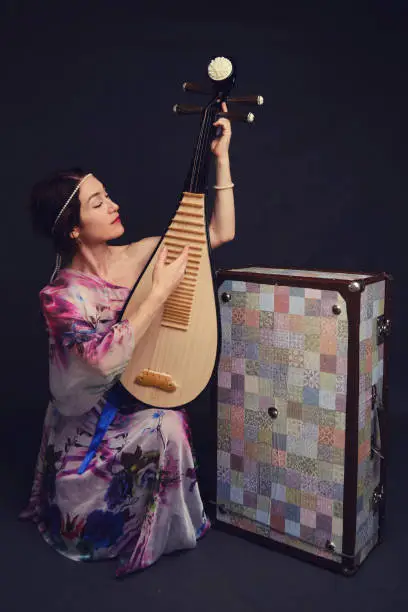 A happy female musician in Asian clothes on a studio black background. A smiling woman with a stringed musical instrument from Asia on a dark background