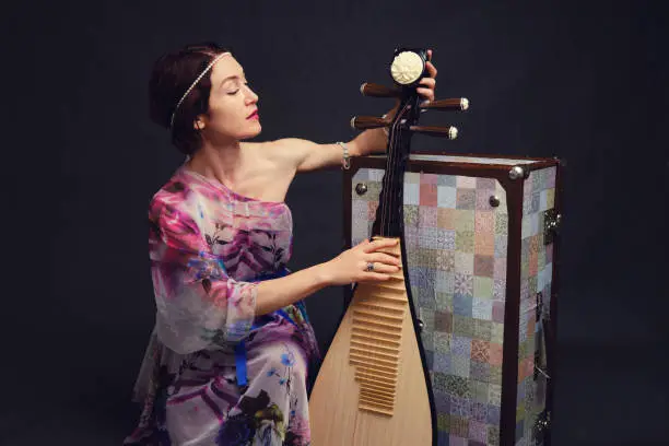 A happy female musician in Asian clothes on a studio black background. A smiling woman with a stringed musical instrument from Asia on a dark background