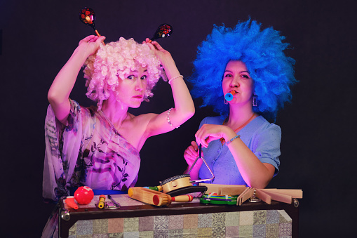 Happy women in funny wigs give a musical performance on a studio black background. Smiling women showing a humorous show on a dark background