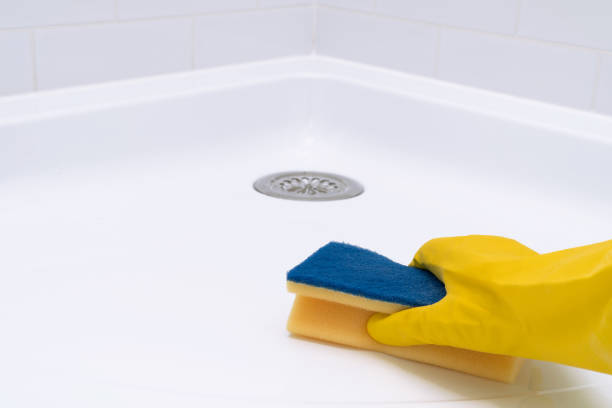 istock Hand in yellow rubber glove scrubbing acrylic shower tray using sponge. 1407264617