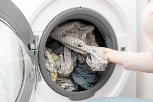 istock Washing machine with clean laundry. Woman hand pulling out washed bed linen from drum of washing machine. 1407264782