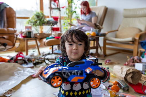 Medium shot of a multiracial toddler boy in his living room in his home in Hexham, Northumberland in the North East of England on Christmas morning. He is handing a toy car to the camera.