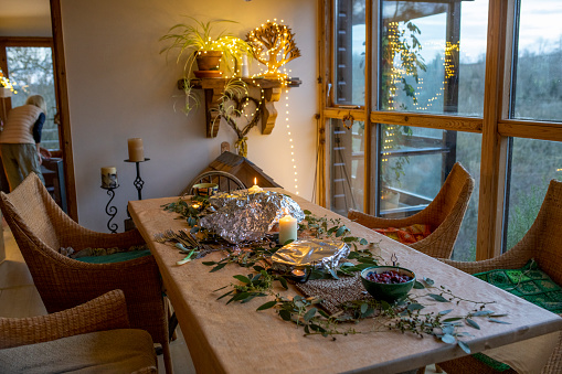 A wide shot of a dining table decorated with eucalyptus branches and candles on Christmas evening.